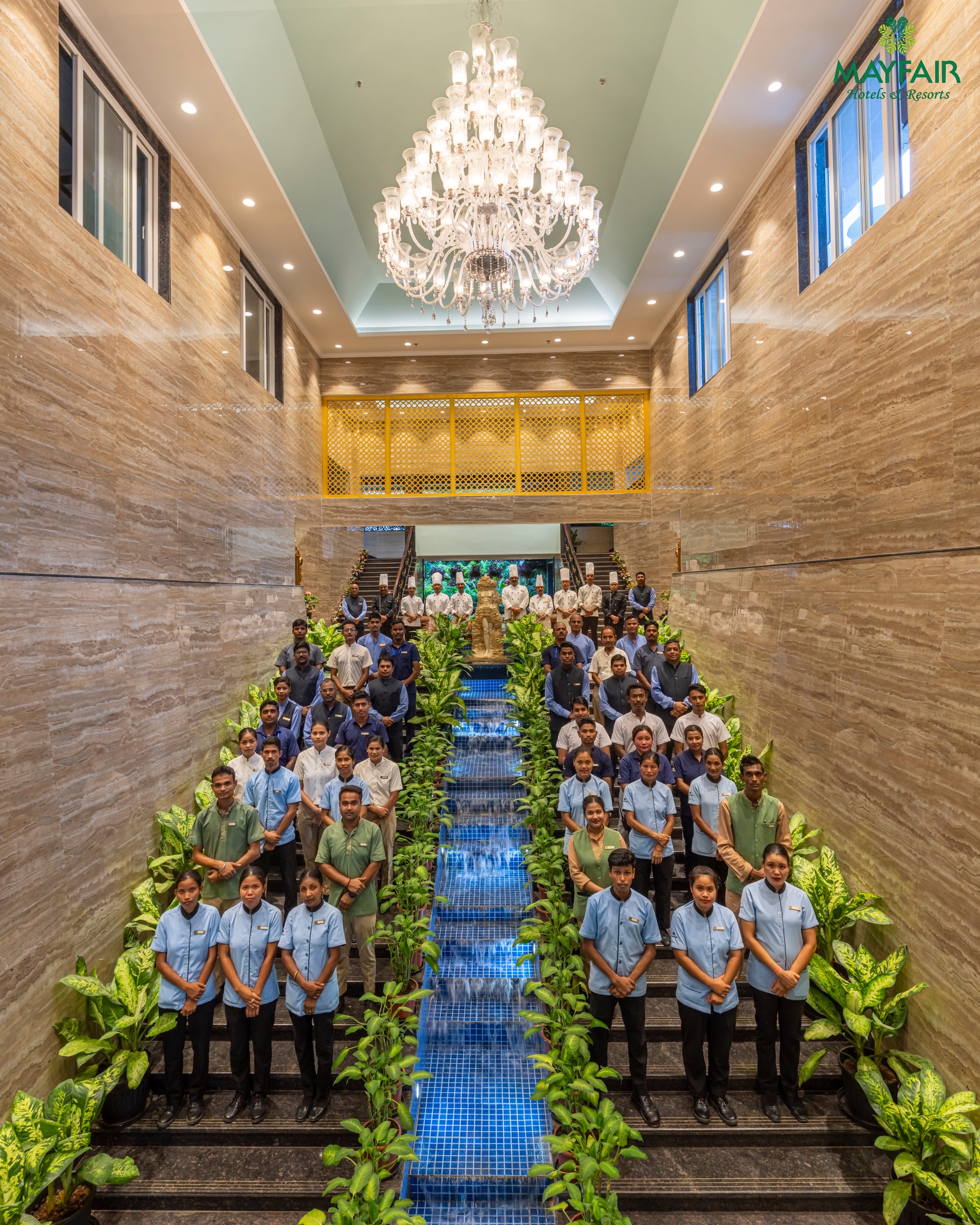 A MAYFAIR team gathered on a staircase beneath a chandelier