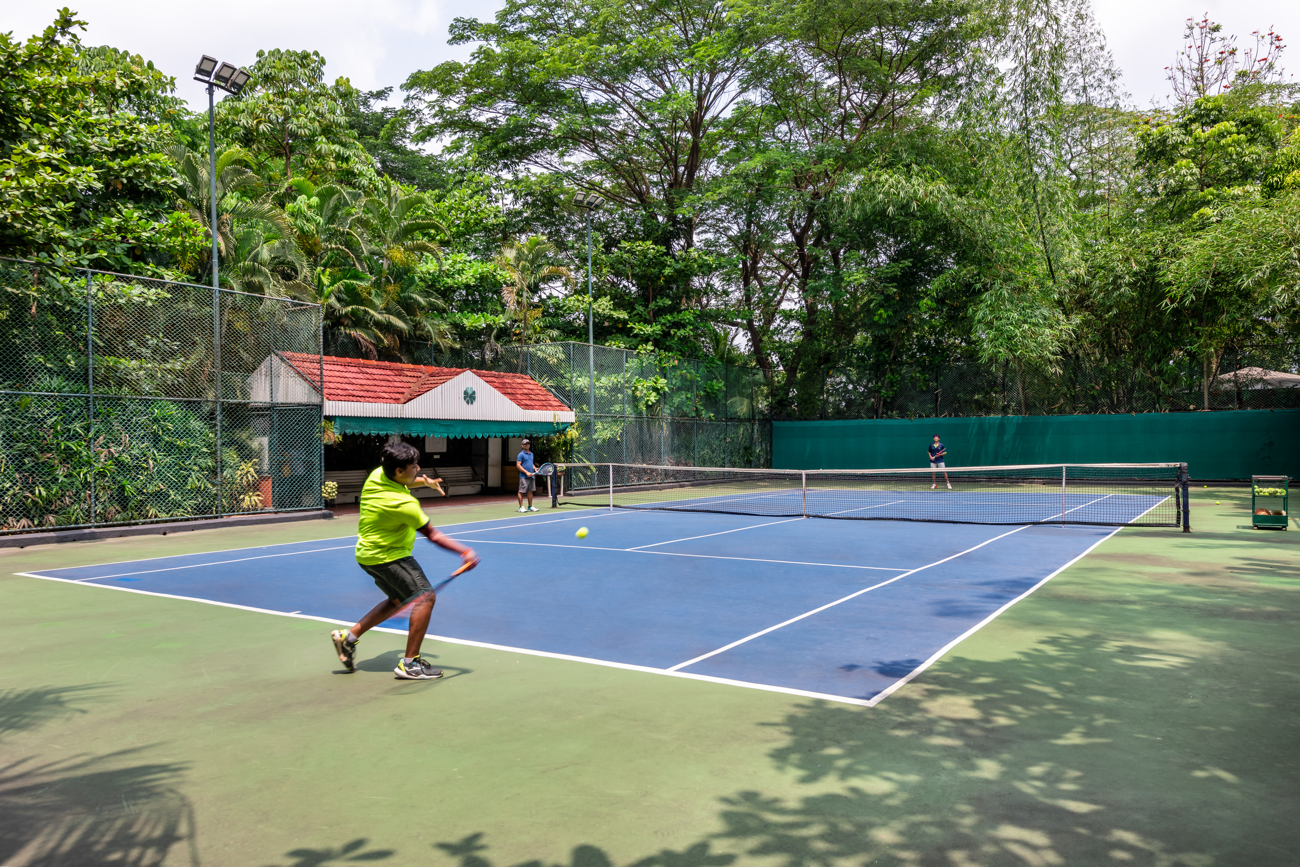 A guest returning a shot on the tennis court at Mayfair Lagoon, the pavilion and trees behind
