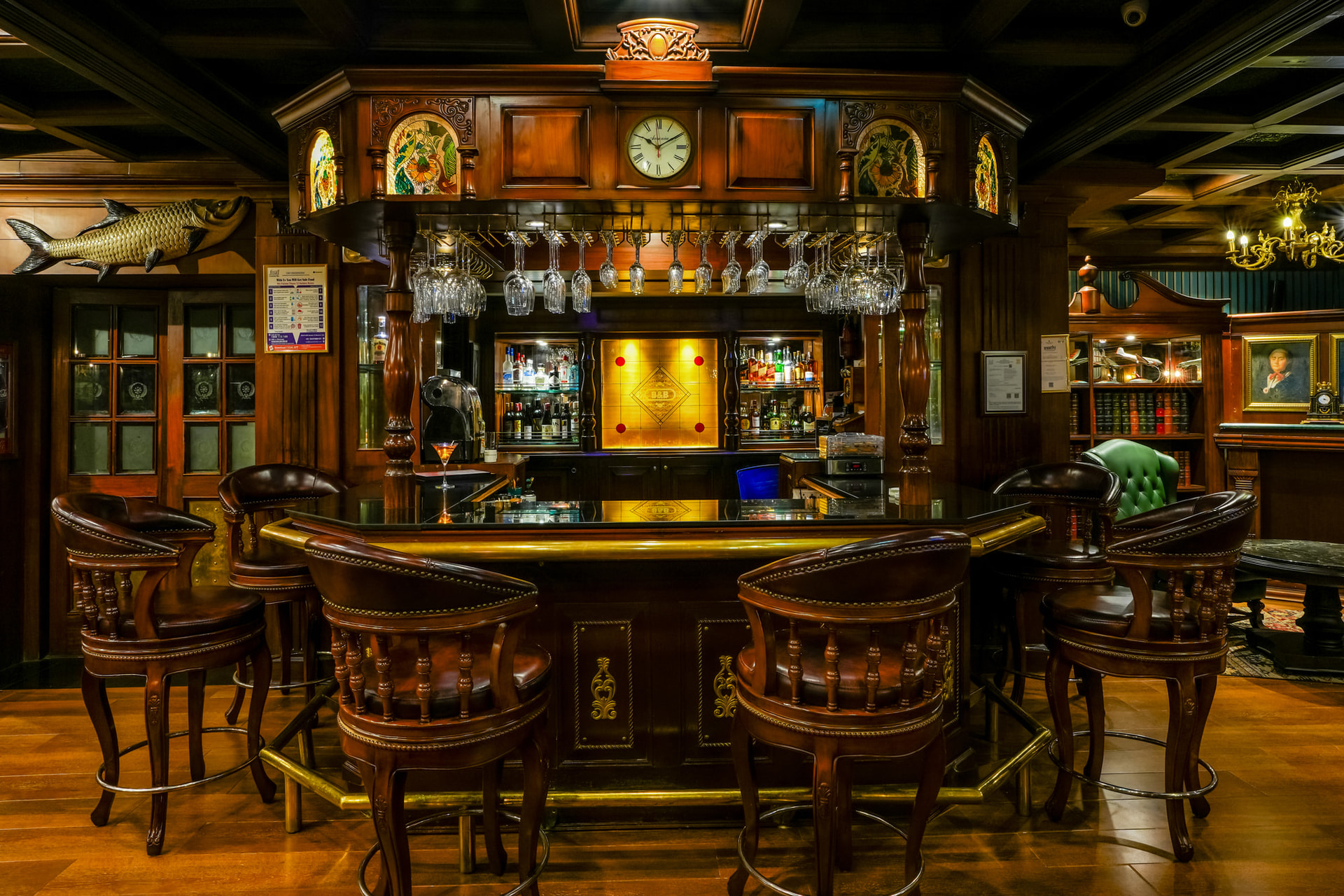 Baron and Baroness bar at MAYFAIR Lagoon, Bhubaneswar featuring a bar counter, liquor bottle in shelves behind the bar, and near the counter top there are chairs placed.
