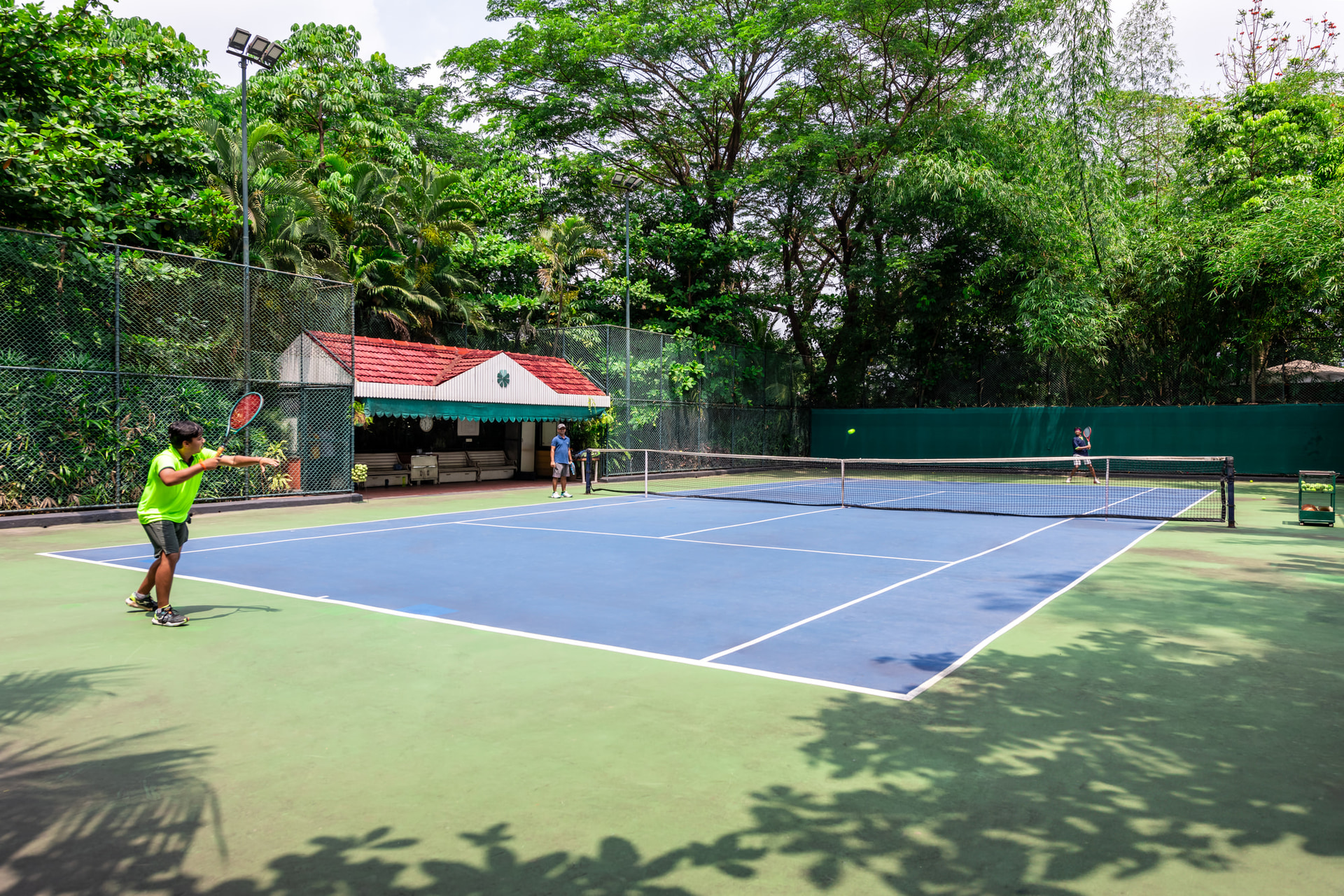 Outdoor tennis court at Mayfair Lagoon, Bhubaneswar, surrounded by lush green trees, offering guests a refreshing sporting experience in a natural setting