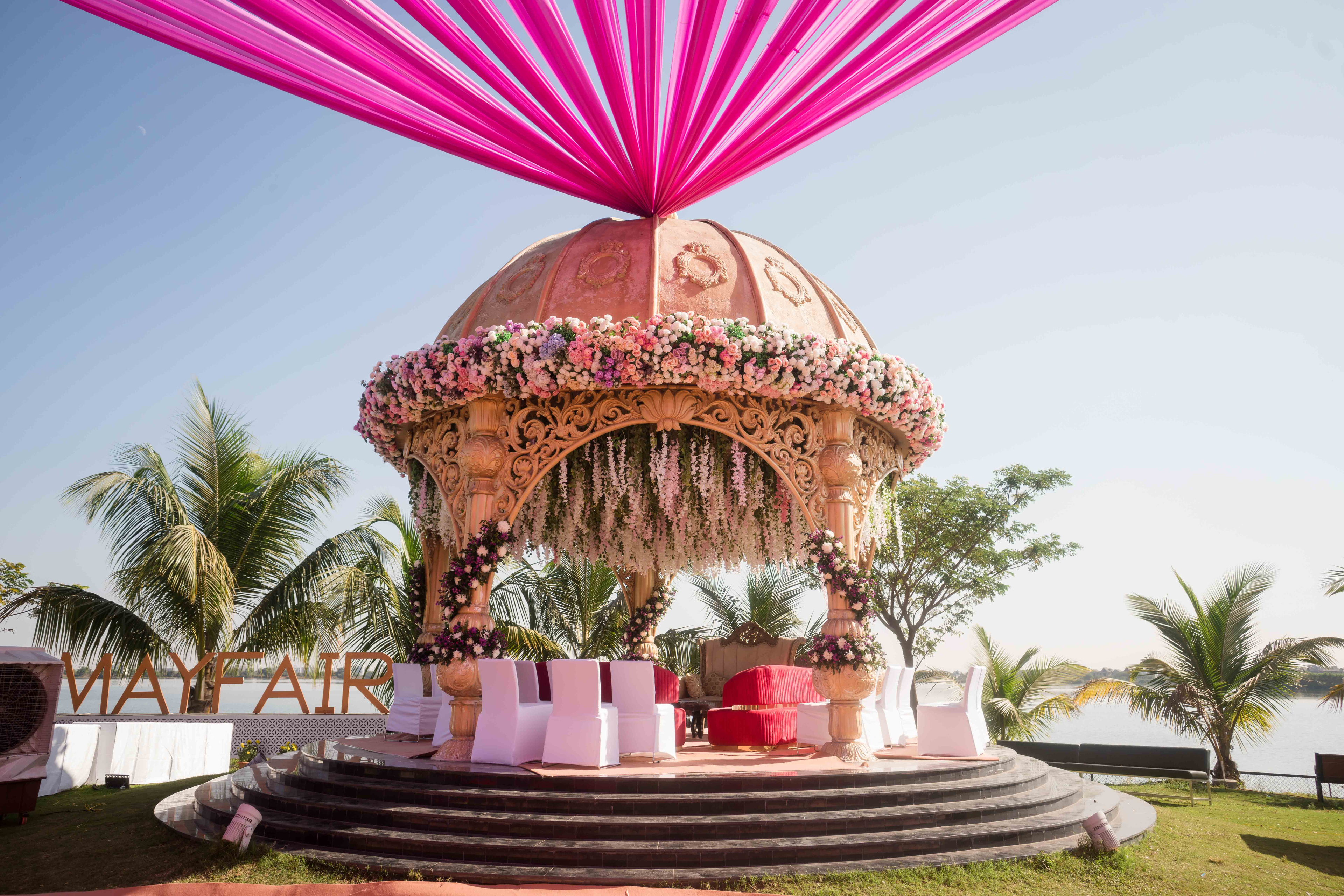 A carved mandap under pink drapes on a lakeside lawn at a MAYFAIR wedding